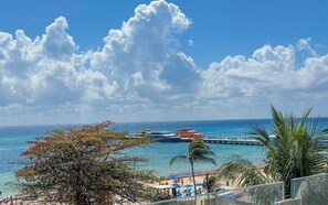 A beach view with a clear sky, palm trees, and a pier with boats. - Grand Boréna Hotel Boutique (Playa del Carmen)