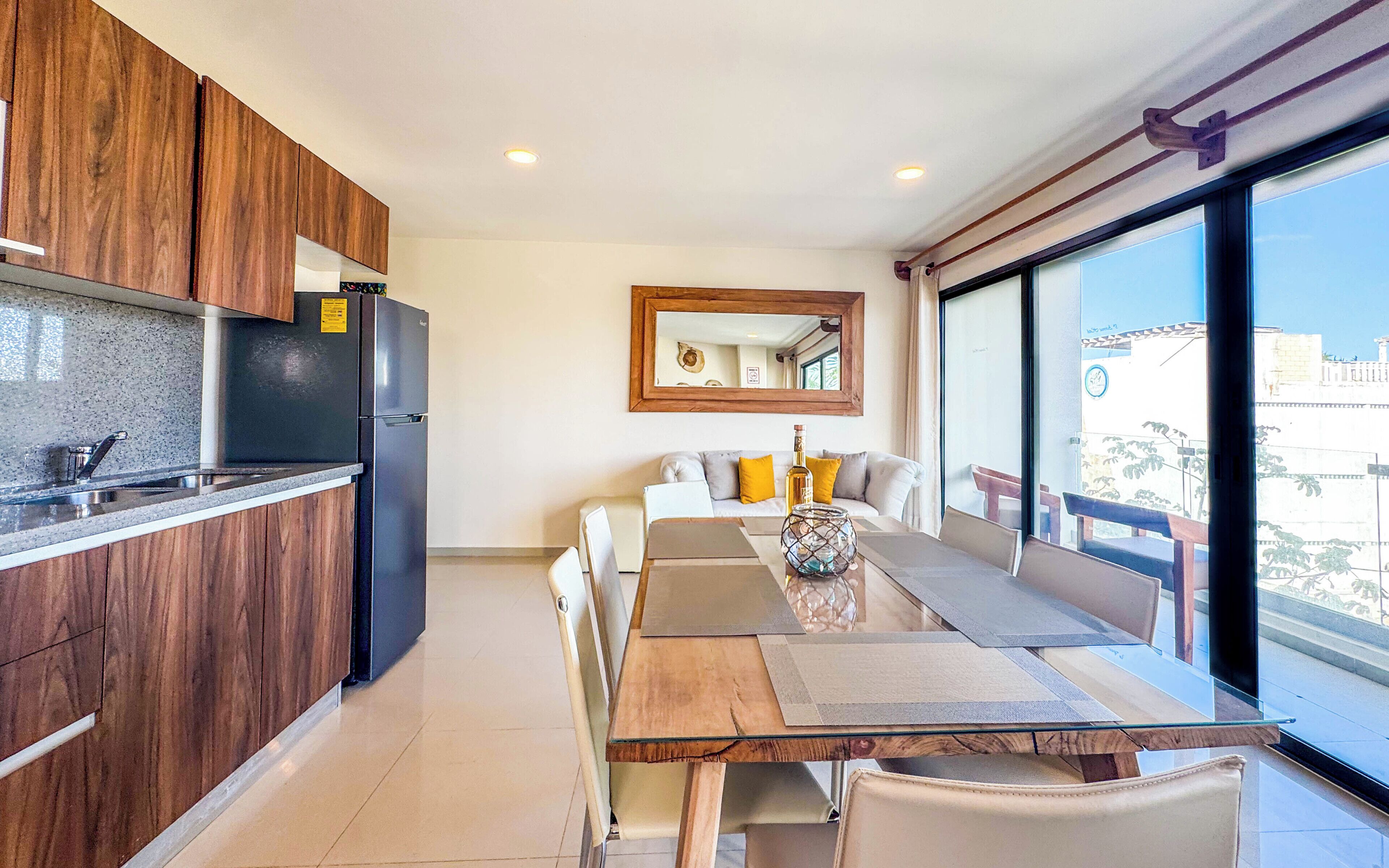 A modern kitchen with wooden cabinets, a built-in refrigerator, and a dining area with a glass table and chairs.
