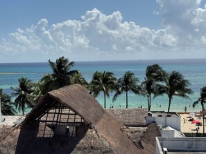 A beach view with palm trees, a thatched-roof structure, and a sandy beach. - Grand Boréna Hotel Boutique (Playa del Carmen)