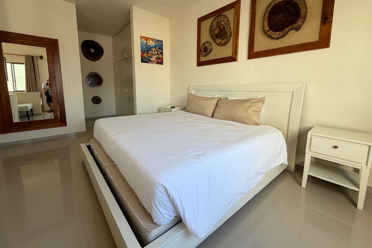 A bedroom with a large bed, a bedside table, a mirror, and artwork on the wall.