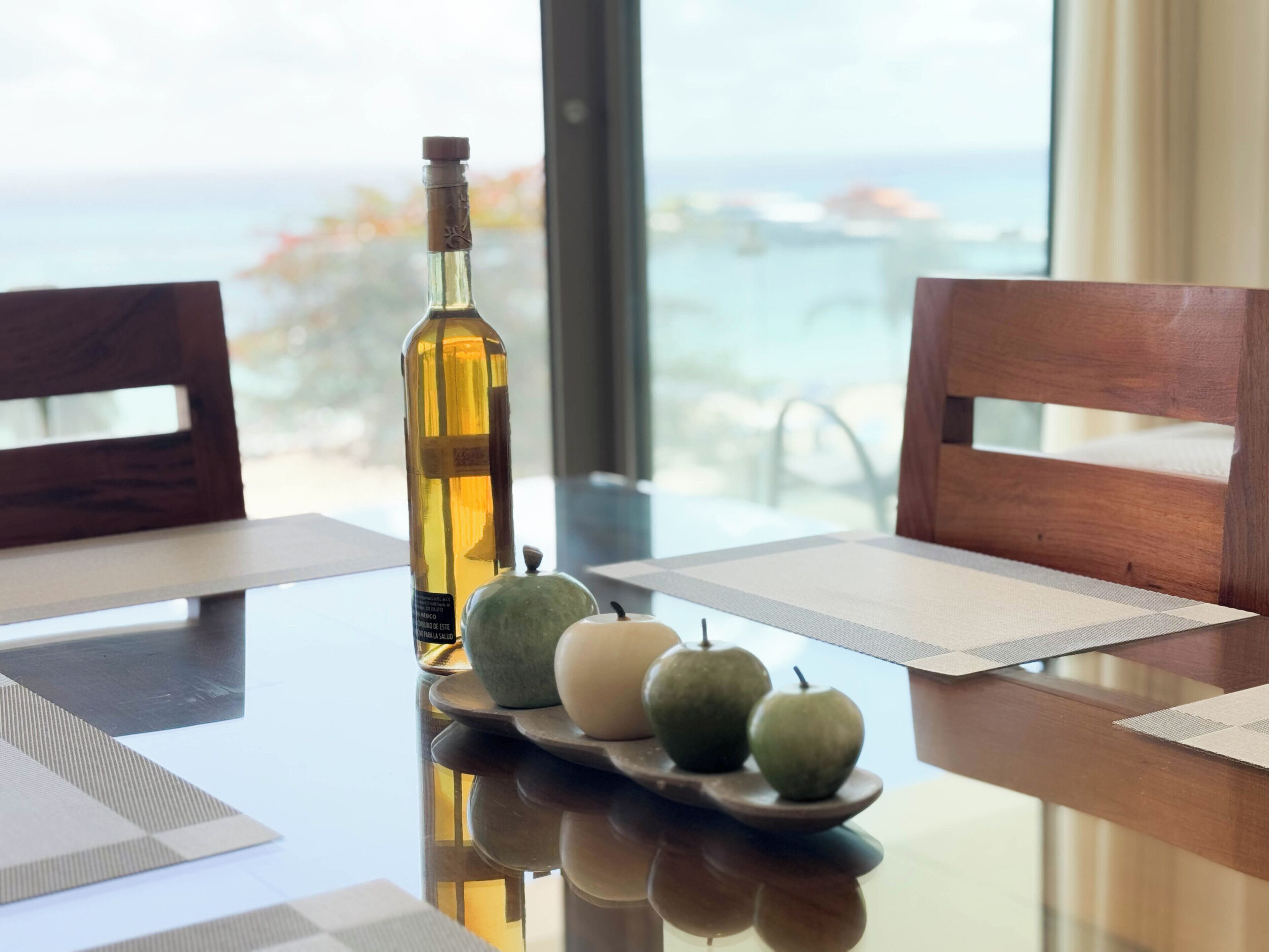 A dining table with a bottle, two apples, and placemats.
