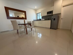 A modern kitchen with white cabinets, a microwave, and a refrigerator. There is a dining table with chairs and a large mirror above it. - Grand Boréna Hotel Boutique (Playa del Carmen)