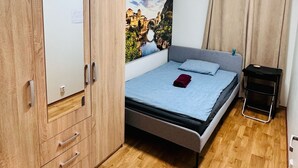 Een slaapkamer met een bed, een houten garderobe, een schilderij aan de muur en een raam met gordijnen.