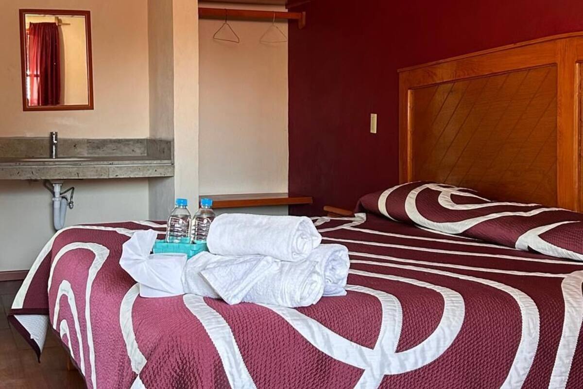 A hotel room with a wooden bed, a mirror, a sink, and a red wall.