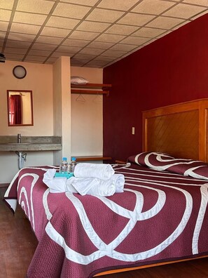 Ein Hotelzimmer mit einem hölzernen Bett, einem Spiegel, einem Waschbecken und einer roten Wand.
