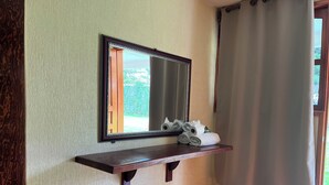 Ein Badezimmer mit einem hölzernen Regal, das Handtücher und einen Spiegel beherbergt, mit Blick auf Grünflächen draußen.