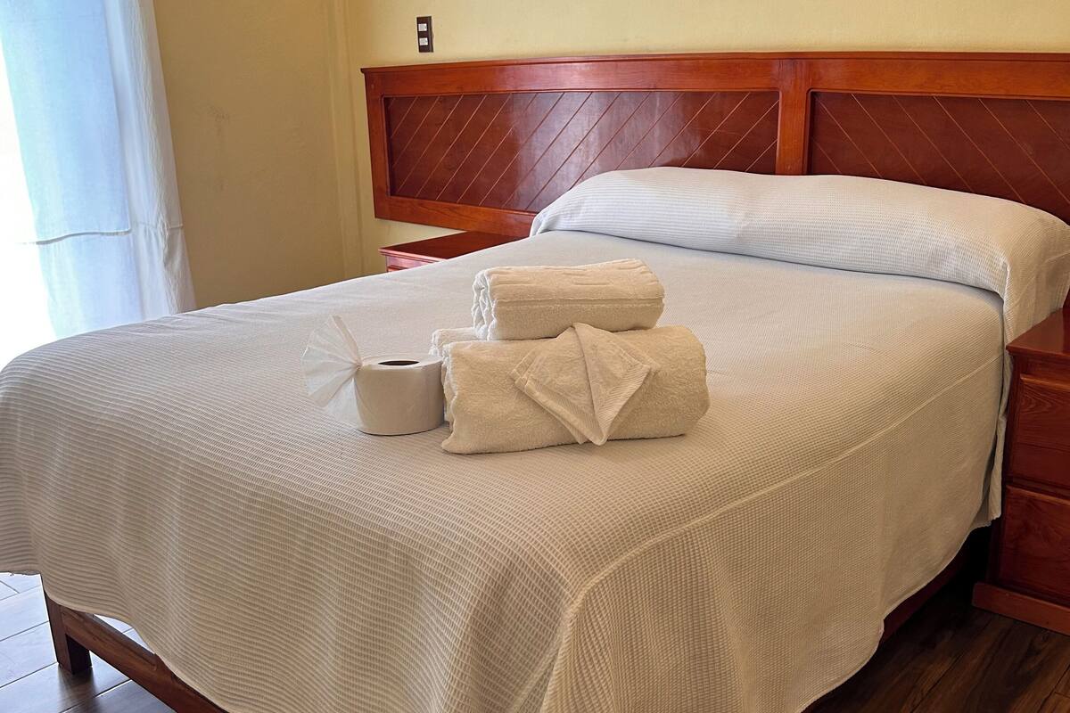 A neatly made bed with a wooden headboard, a white bedspread, and a set of towels on the bed.