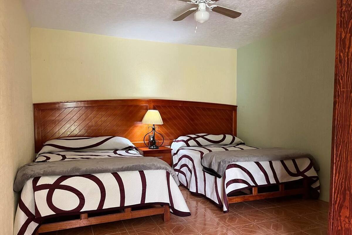 A room with two beds, a wooden headboard, a lamp, and a ceiling fan.