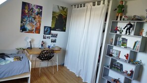 Un dormitorio con cama, escritorio, silla y estanterías llenas de objetos de colección.