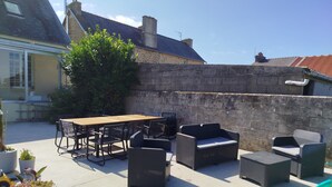 Un patio al aire libre con mesa y sillas de madera, sofás de mimbre y plantas en macetas.