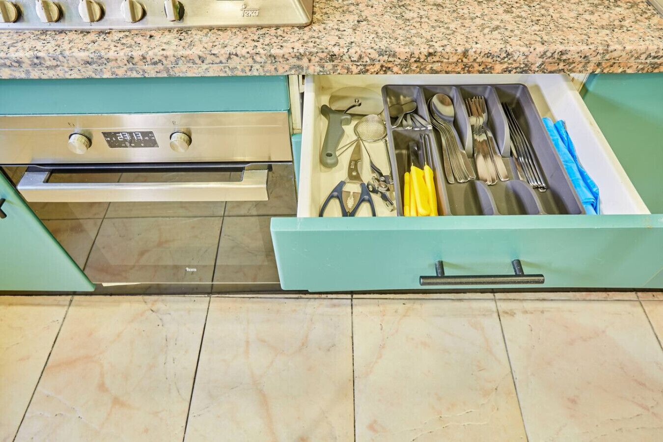 Une cuisine avec un tiroir de couleur turquoise contenant des ustensiles et un four en acier inoxydable.