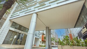Un bâtiment moderne doté d’une façade en verre, d’une entrée couverte et d’un palmier au premier plan.