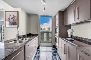 A modern kitchen with granite countertops, stainless steel appliances, and a view of the cityscape through an open door. - Sky-High Water Views | Icon Brickell 2BR (Miami)