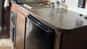 A compact kitchen with a built-in oven, microwave, and dishwasher. There is a sink with a faucet, and a countertop with a few items on it. - Cozy RV Camper in tranquil Brandon near everything (Brandon)