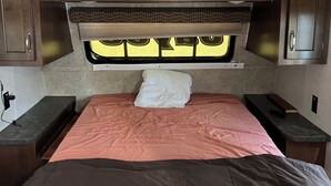 A compact RV interior with a bed, two bedside tables, and overhead cabinets. - Cozy RV Camper in tranquil Brandon near everything (Brandon)