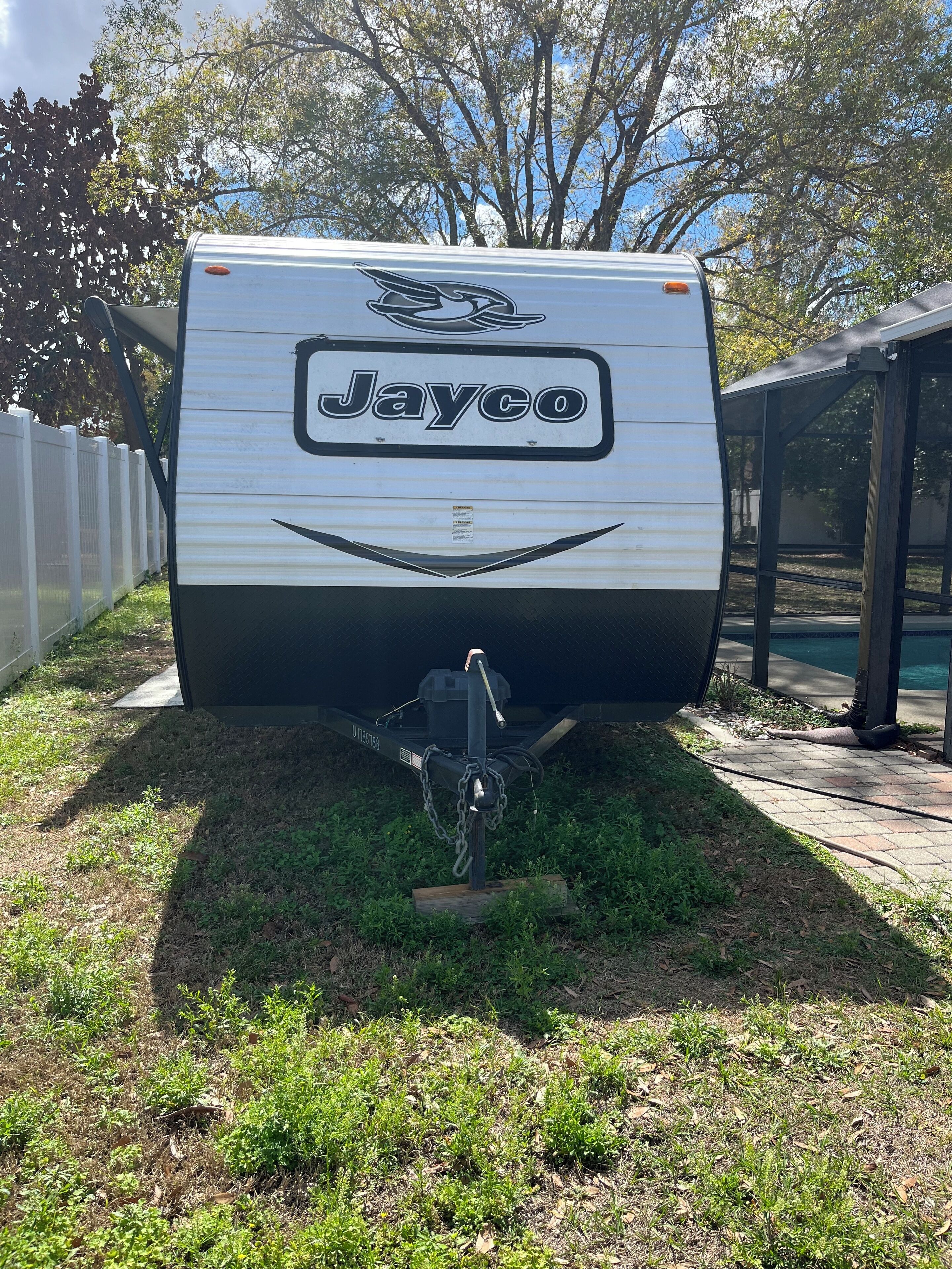 Un camper Jayco parcheggiato in una zona erbosa, con una recinzione bianca e alberi sullo sfondo.