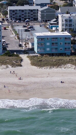 Una playa con edificios al fondo, incluyendo un edificio azul de varios pisos y balcones.