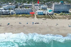Une vue aérienne d’une plage avec un panneau indiquant « Accès à la plage », des bâtiments et une vue sur l’océan.