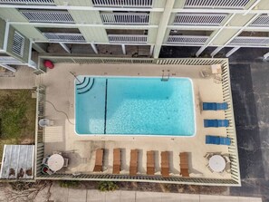 Vista aérea de una piscina rectangular con agua cristalina, rodeada por una terraza con sillas de descanso y una pequeña mesa.