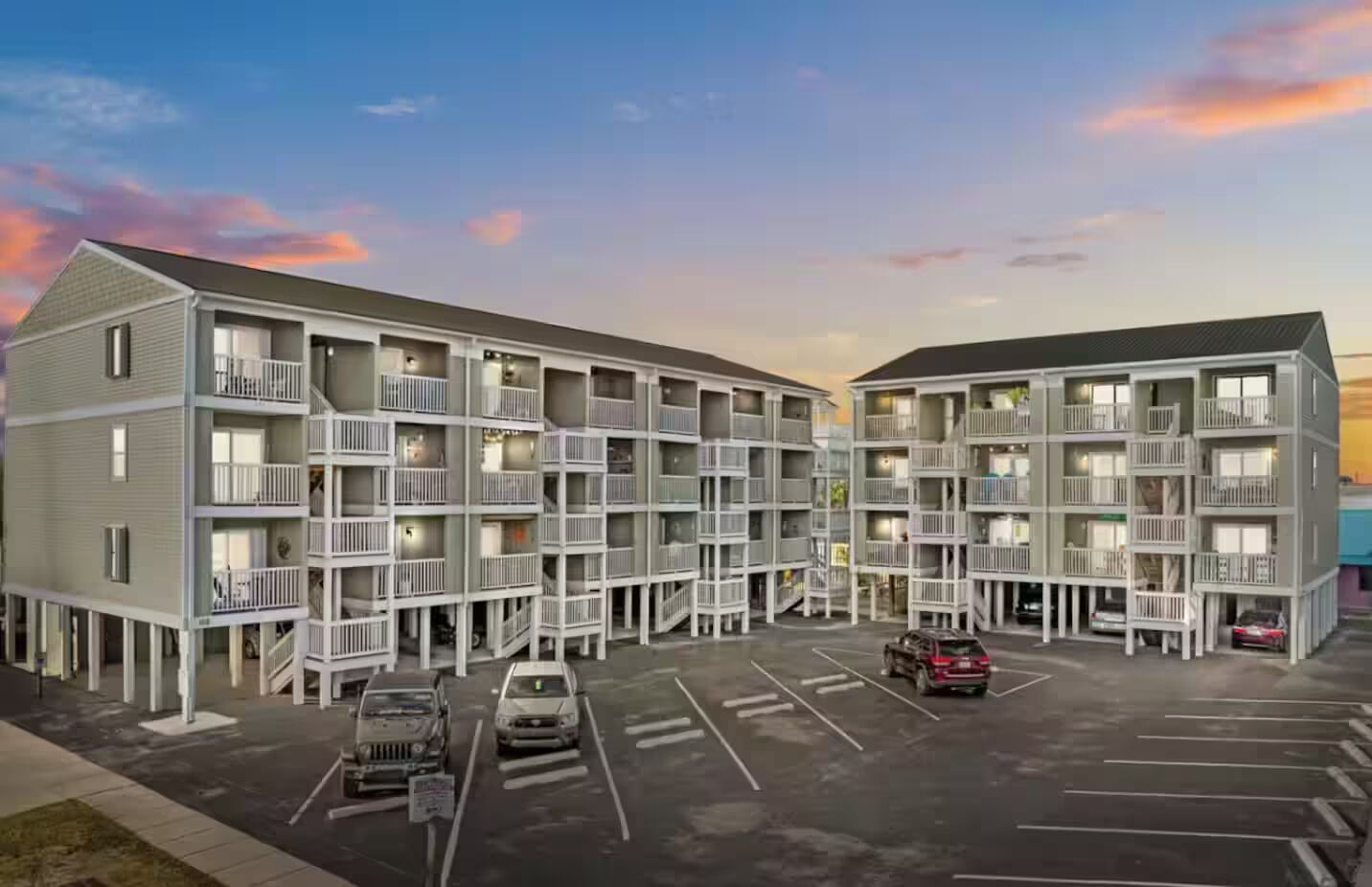 Ein mehrstöckiges Hotel mit Balkonen, einem Parkplatz und einem Sonnenuntergangshimmel.