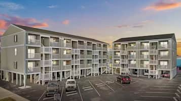 Ein mehrstöckiges Hotel mit Balkonen, einem Parkplatz und einem Sonnenuntergangshimmel.