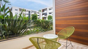 Ein Balkon mit zwei grünen Korbstühlen und einem kleinen Tisch, mit Blick auf einen Garten und ein weißes Gebäude mit Balkonen.