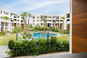 A modern hotel courtyard with a central swimming pool, surrounded by lush greenery and palm trees. - Modern 2BR Duplex in Bouskoura | Pool Access | Parking (Casablanca)