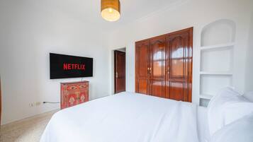 Une chambre à coucher avec un grand lit, une armoire, un téléviseur fixé au mur et un luminaire suspendu.