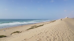 Une plage de sable où l’on peut voir des empreintes de pas menant à l’eau, quelques personnes et des tentes installées sur les dunes.