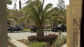 A parking area with several vehicles, including a jet ski, a motorcycle, and an ATV, surrounded by palm trees and a stone wall.