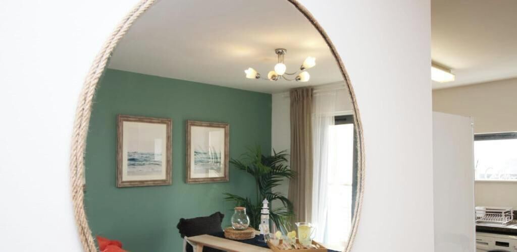 A room with a dining table, chairs, a mirror, two framed pictures, a plant, and a chandelier.