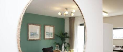A room with a dining table, chairs, a mirror, two framed pictures, a plant, and a chandelier.