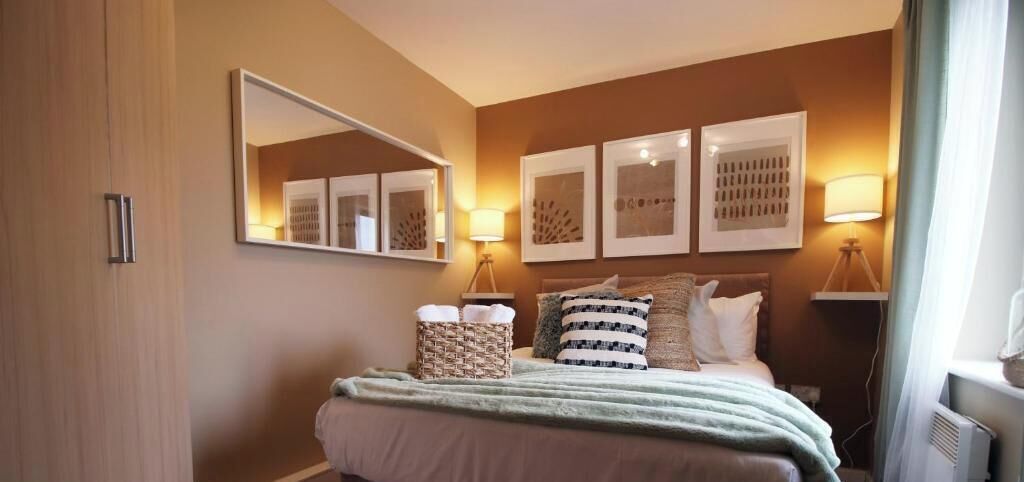 A hotel room with a bed, a large mirror, wall art, and bedside lamps.