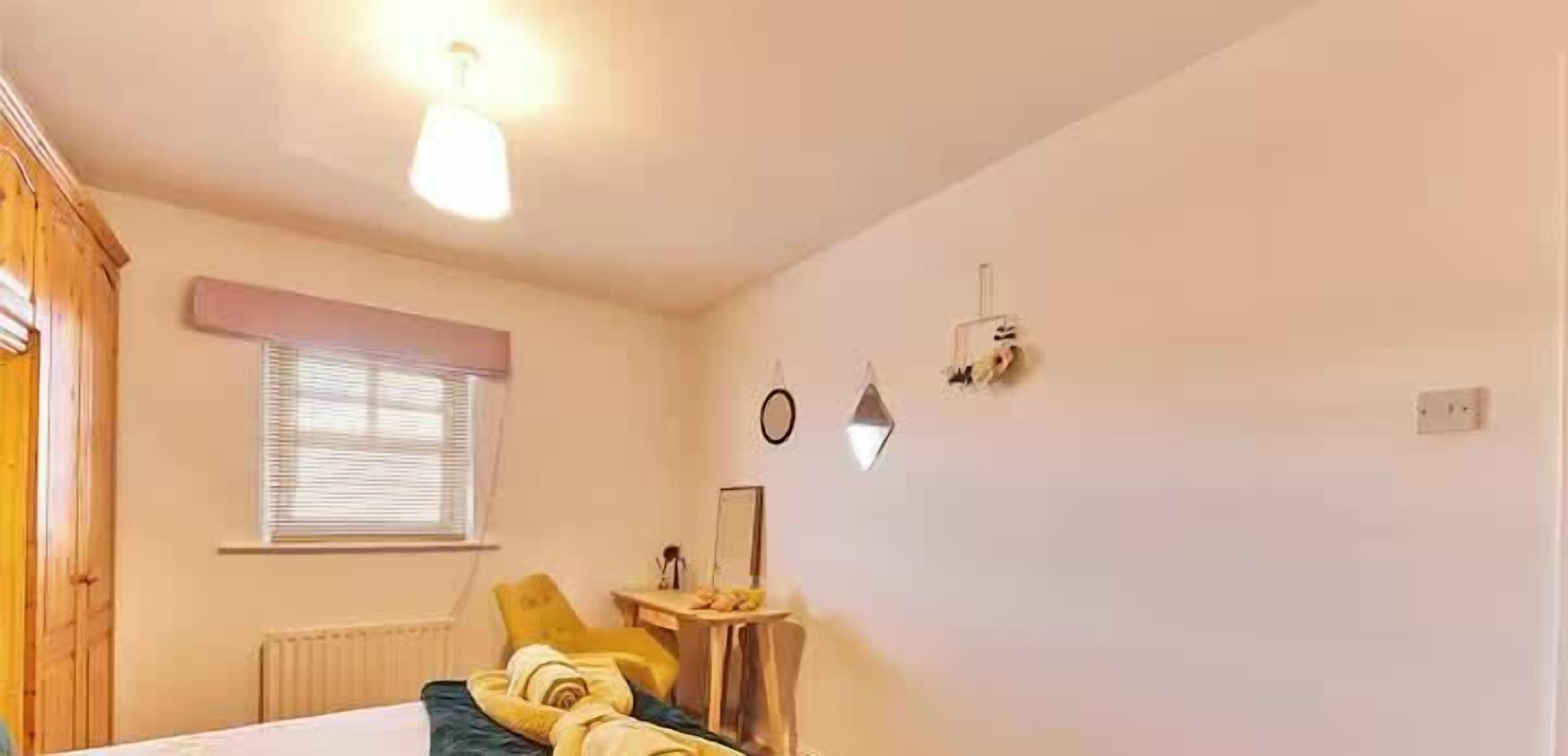 Ein Schlafzimmer mit einem Bett, einem Nachttisch, einem Fenster mit Jalousien, einer Heizung und einer Wandleuchte.