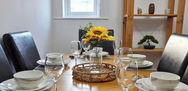 A dining table set with plates, bowls, and wine glasses, accompanied by a vase of sunflowers and a bonsai tree. - Stylish 2Bed Flat - Contractors & Family - Parking (Tyne and Wear)