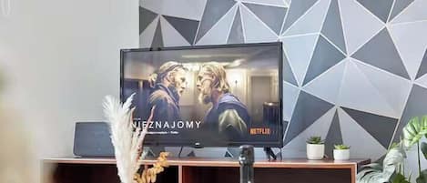 Un televisor mostrando una película con el logotipo de Netflix, un mueble de madera debajo y un diseño geométrico en la pared.