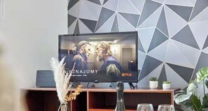 A television displaying a movie with the Netflix logo, a wooden entertainment unit below, and a geometric wall pattern. - Modern 2Bed Home - Contractors & Family - Parking (Tyne and Wear)