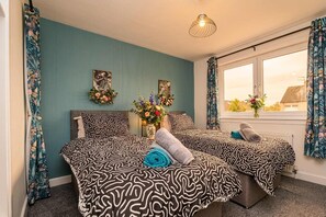A bedroom with two beds, floral curtains, a window with a view, and a hanging light fixture.