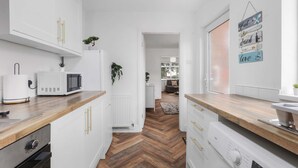 A modern kitchen with white cabinetry, a microwave, and a wooden countertop. There is a plant on the countertop and a hanging sign on the wall. - Contractor Stay - WI-Fi - Pet Friendly - Parking (Consett)