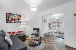 A modern living room with a sofa, armchair, coffee table, and a painting of deer. - Contractor Stay - WI-Fi - Pet Friendly - Parking (Consett)