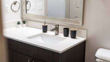 A modern bathroom with a white sink, dark wood cabinets, a large mirror, and two black cups on the counter.