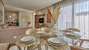 A modern living room with a glass dining table set for four, a sofa, and a TV displaying "NETFLIX". - Luxury 3-Bedroom Getaway in Bouskoura`s Finest (Bouskoura)