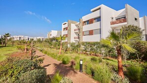 A modern residential building with a flat roof, large windows, and a well-maintained garden with palm trees and shrubs. - Luxury 3-Bedroom Getaway in Bouskoura`s Finest (Bouskoura)