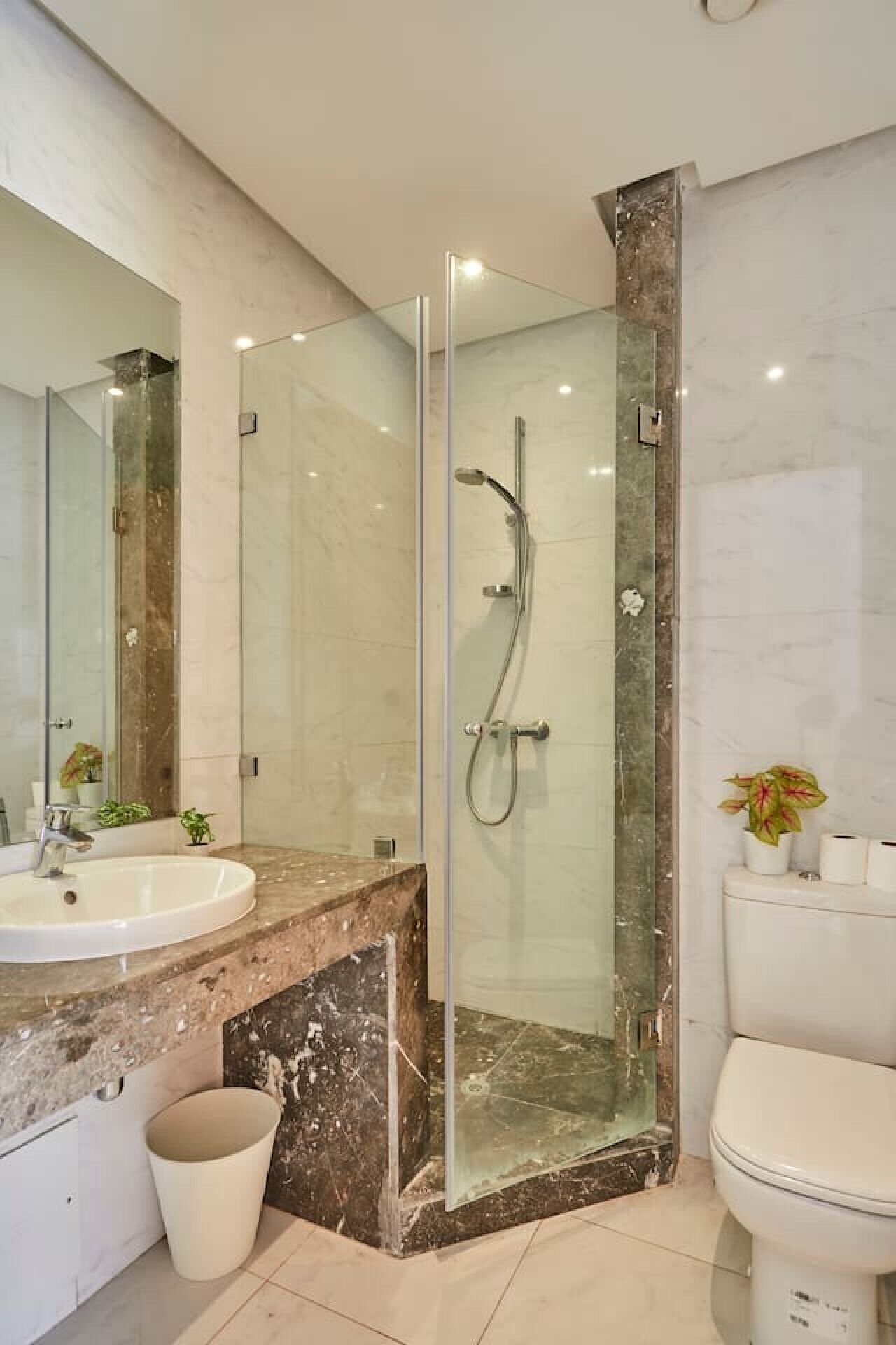 Un baño moderno con ducha envuelta en vidrio, lavamanos de mármol y un inodoro.