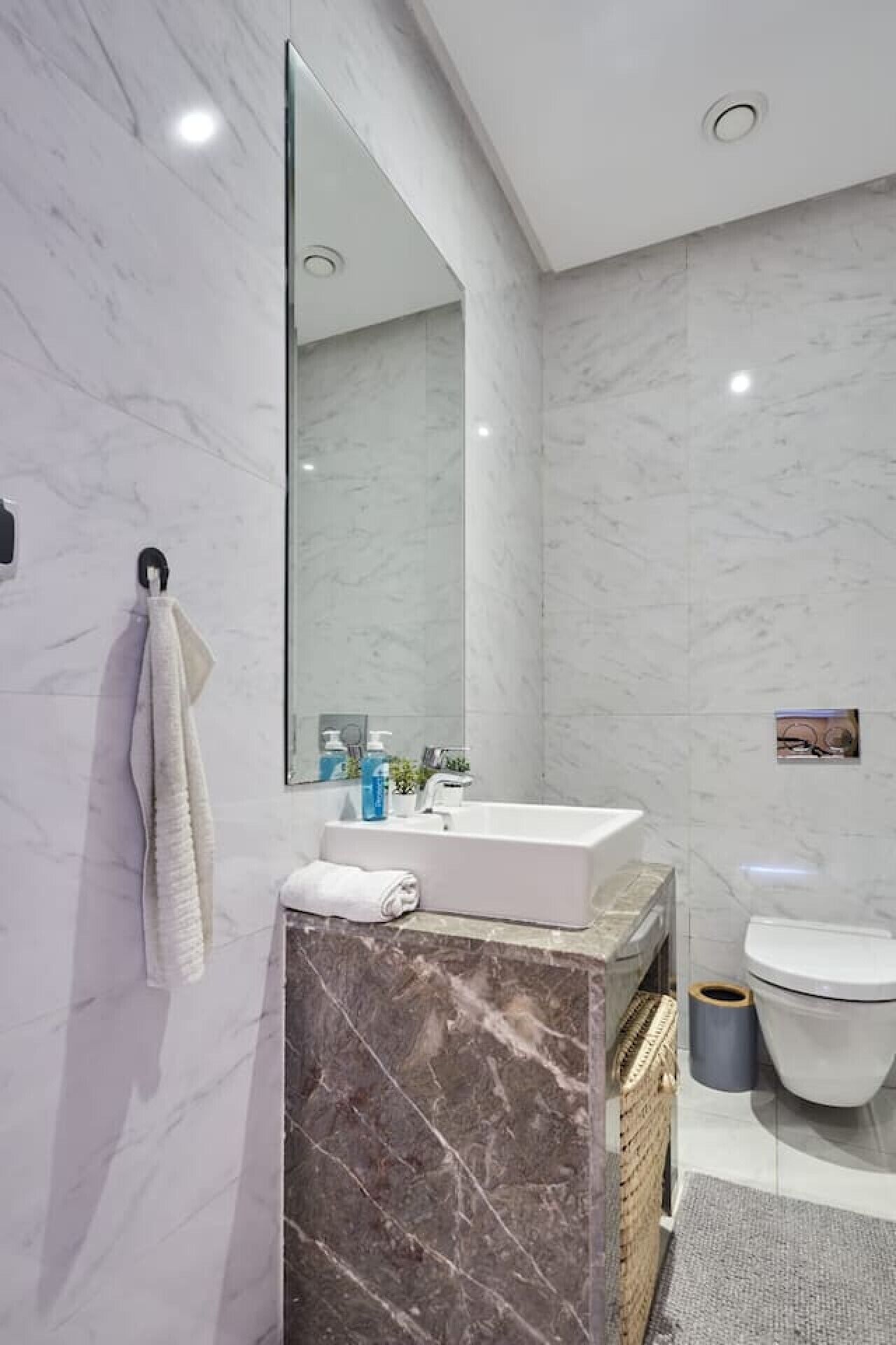A modern bathroom with a marble vanity, a large mirror, a toilet, and a towel rack.