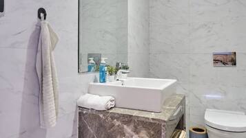 A modern bathroom with a marble vanity, a large mirror, a toilet, and a towel rack.
