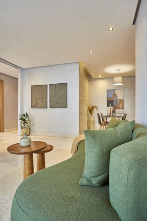 A modern living room with a green sofa, a small wooden table, and two abstract paintings on the wall. - Family-Friendly 3BR with Garden & Outdoor Space (Bouskoura)
