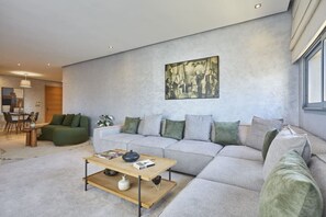 A modern living room with a grey sectional sofa, a wooden coffee table, and a painting on the wall.