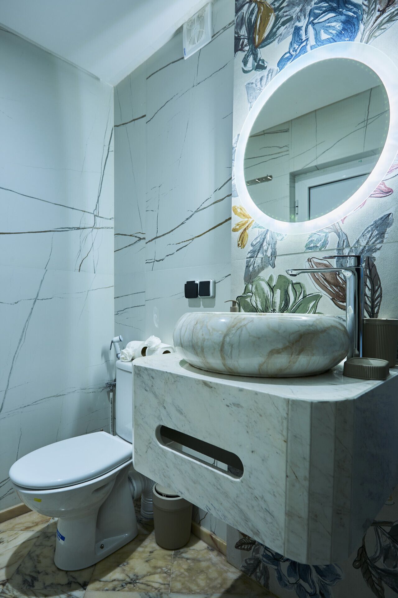 Ein Badezimmer mit Marmorwaschbecken, Toilette und einer Wand mit floralem Wandbild.