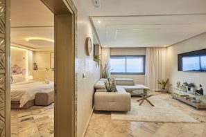 Een moderne woonkamer met een bank, een glazen salontafel en een aan de muur bevestigde televisie.